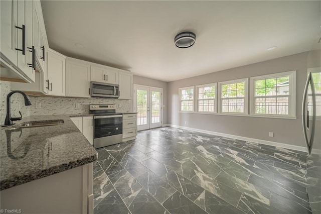 kitchen with white cabinetry, stainless steel appliances, sink, and dark stone countertops