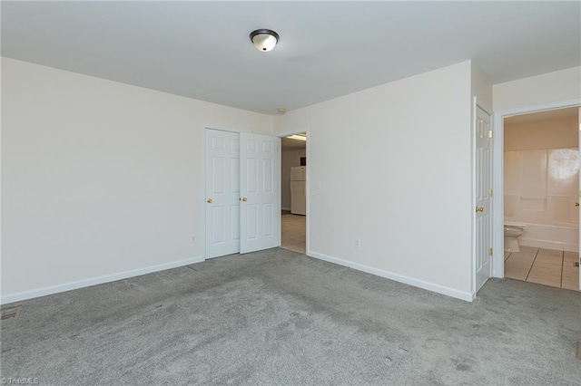 unfurnished bedroom with baseboards, carpet, ensuite bathroom, and freestanding refrigerator