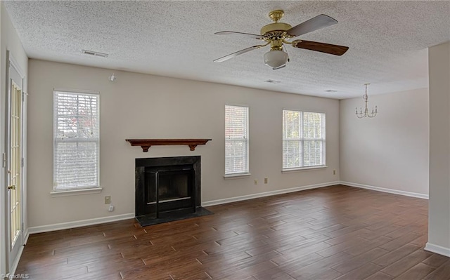 unfurnished living room featuring ceiling fan with notable chandelier, a textured ceiling, a wealth of natural light, and dark wood-type flooring