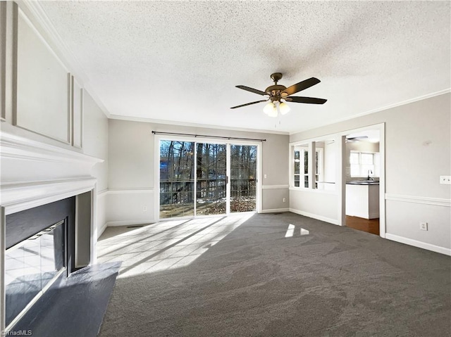 unfurnished living room with a textured ceiling, dark colored carpet, ceiling fan, and crown molding