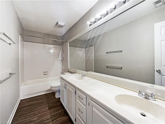 full bathroom with wood-type flooring, toilet, tub / shower combination, vanity, and a textured ceiling