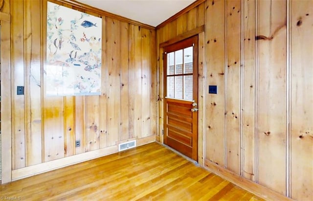 doorway with ornamental molding, light wood-type flooring, visible vents, and wooden walls