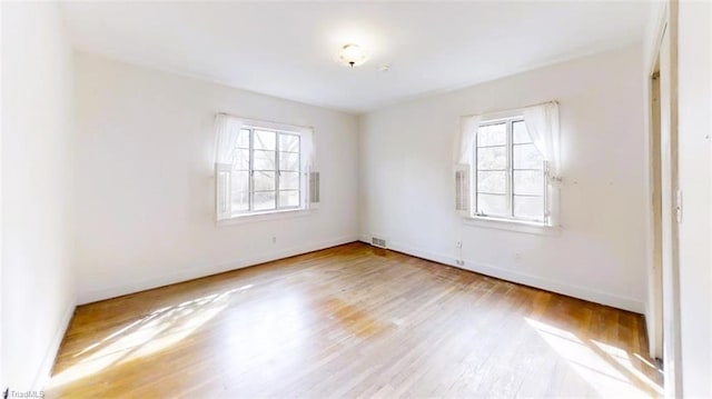 spare room featuring wood finished floors, visible vents, and baseboards