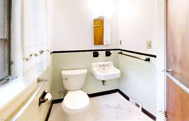 half bathroom with a wainscoted wall, visible vents, a sink, and toilet