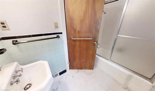 full bathroom featuring marble finish floor, enclosed tub / shower combo, a sink, and tile walls