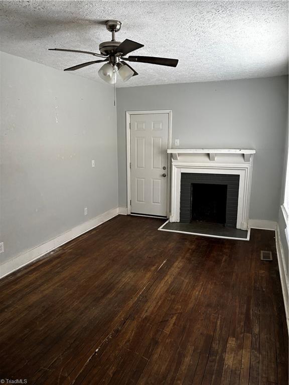 unfurnished living room with ceiling fan, dark hardwood / wood-style flooring, a brick fireplace, and a textured ceiling