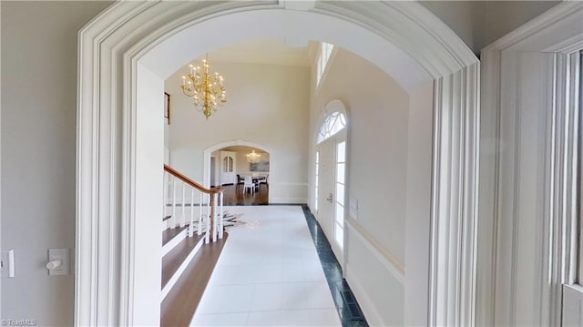 hall featuring arched walkways, tile patterned flooring, a chandelier, stairs, and french doors