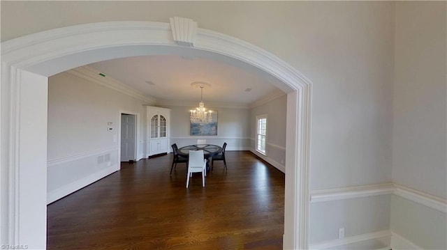 dining space with dark wood-type flooring, arched walkways, a notable chandelier, and crown molding