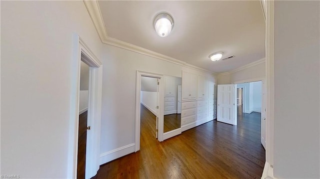 corridor featuring dark wood-type flooring, ornamental molding, baseboards, and visible vents