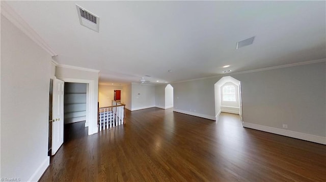 empty room with dark wood-type flooring, visible vents, baseboards, and crown molding