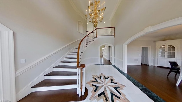 stairway featuring crown molding, arched walkways, a high ceiling, and a chandelier