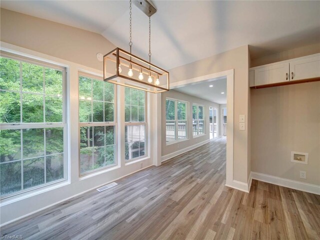 unfurnished dining area featuring a healthy amount of sunlight, vaulted ceiling, a notable chandelier, and light hardwood / wood-style floors