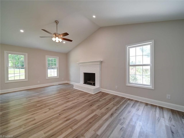 unfurnished living room with a brick fireplace, lofted ceiling, light wood-type flooring, and ceiling fan