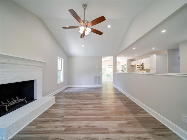 unfurnished living room with lofted ceiling, a healthy amount of sunlight, a brick fireplace, and light wood-type flooring