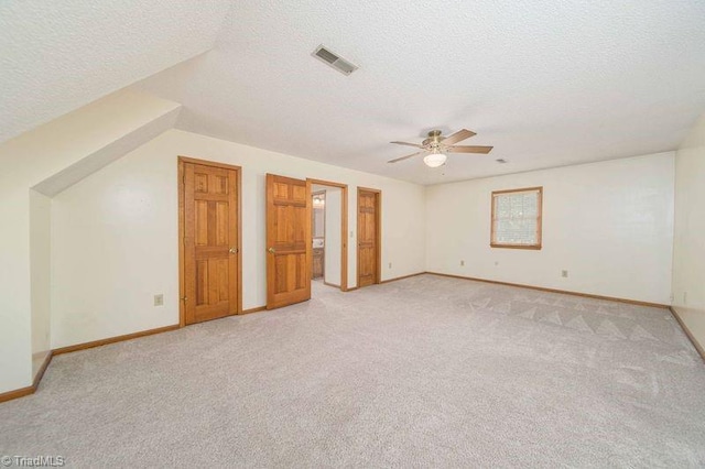 unfurnished bedroom with light colored carpet, a textured ceiling, baseboards, and a ceiling fan