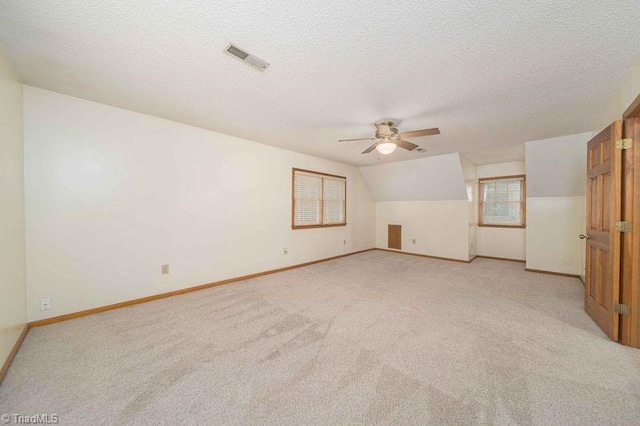 additional living space featuring ceiling fan, light colored carpet, baseboards, and a textured ceiling