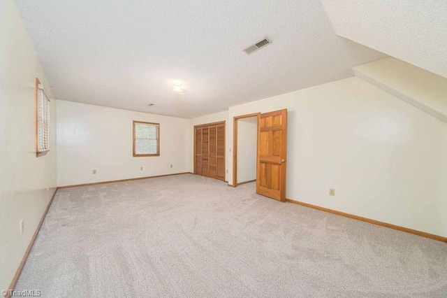 unfurnished bedroom with a textured ceiling, light carpet, baseboards, and a closet