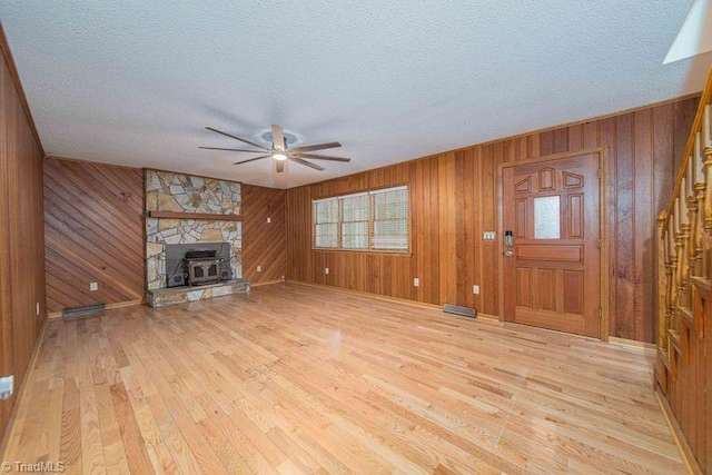 unfurnished living room featuring a ceiling fan, a textured ceiling, light wood-style floors, and wood walls