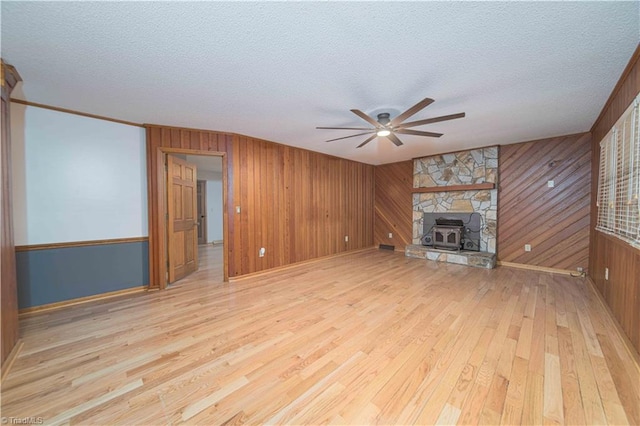 unfurnished living room featuring a ceiling fan, a textured ceiling, light wood-style floors, wood walls, and a stone fireplace