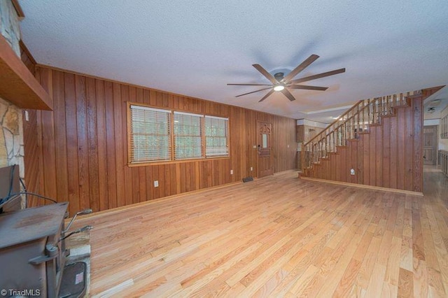 unfurnished living room featuring stairs, wood-type flooring, ceiling fan, a textured ceiling, and wooden walls