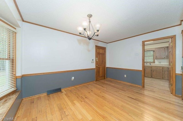 spare room featuring a chandelier, crown molding, light wood-style flooring, and a textured ceiling