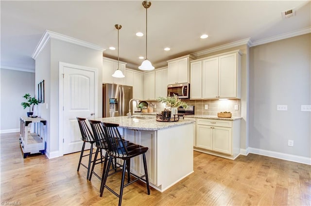 kitchen with stainless steel appliances, tasteful backsplash, light stone counters, an island with sink, and light wood-type flooring