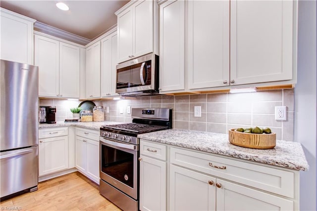 kitchen with light stone countertops, white cabinetry, light hardwood / wood-style floors, and appliances with stainless steel finishes