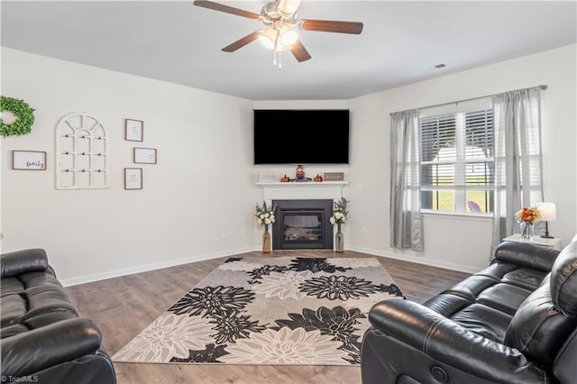 living room with ceiling fan, a glass covered fireplace, baseboards, wood finished floors, and visible vents