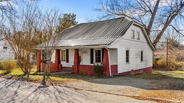 view of front facade featuring metal roof, a standing seam roof, a porch, and brick siding