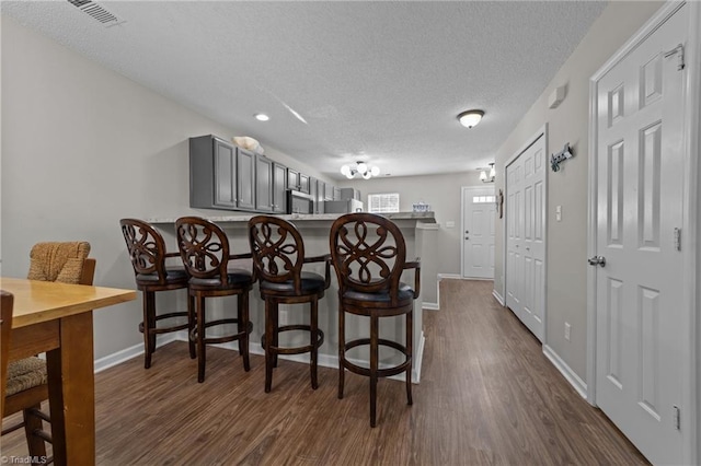 bar featuring dark wood-style floors, a textured ceiling, stainless steel microwave, baseboards, and recessed lighting