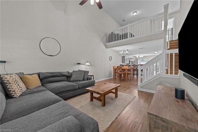 living area with stairway, a ceiling fan, wood finished floors, high vaulted ceiling, and baseboards