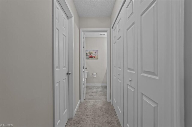 corridor with a textured ceiling, baseboards, and light colored carpet