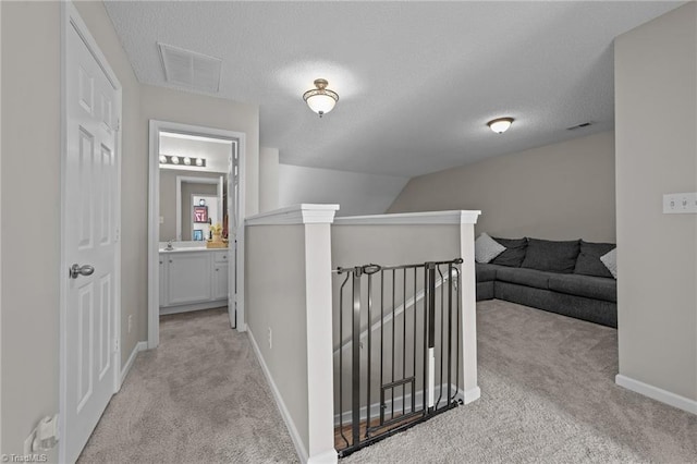 corridor featuring an upstairs landing, light carpet, baseboards, and a textured ceiling