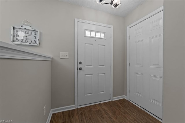 entrance foyer featuring baseboards, a textured ceiling, dark wood-type flooring, and a chandelier