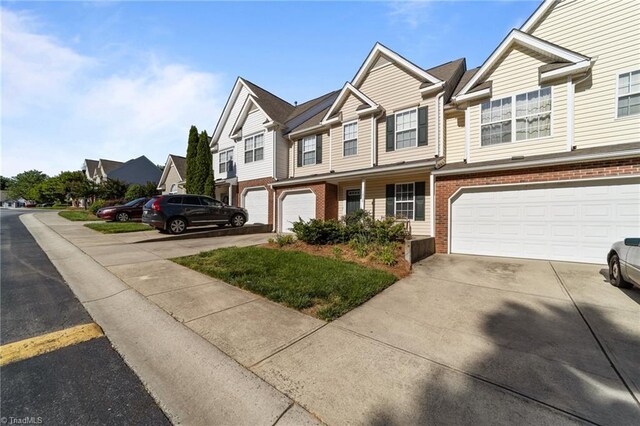 view of property featuring brick siding, driveway, a residential view, and a garage
