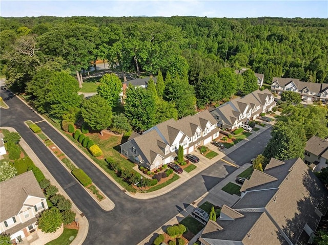 aerial view of property and surrounding area featuring a forest and nearby suburban area