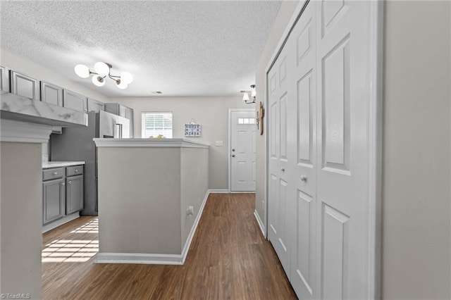 corridor featuring a textured ceiling, dark wood-type flooring, baseboards, and a chandelier