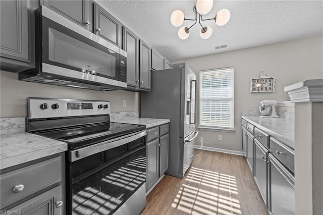 kitchen featuring appliances with stainless steel finishes, a chandelier, gray cabinetry, and a textured ceiling