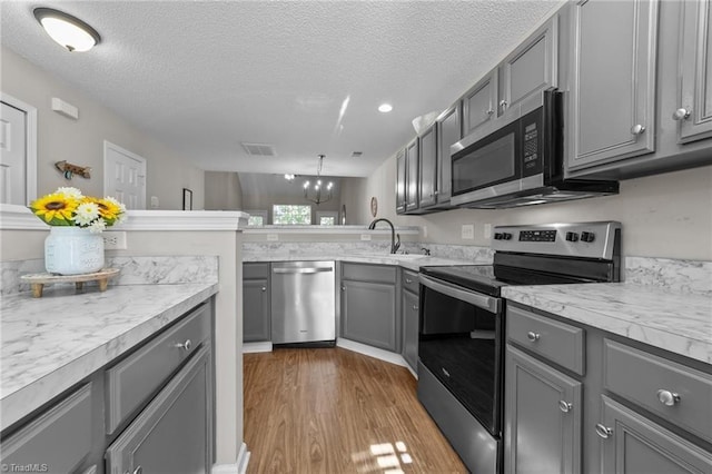 kitchen featuring appliances with stainless steel finishes, gray cabinets, a sink, light countertops, and wood finished floors