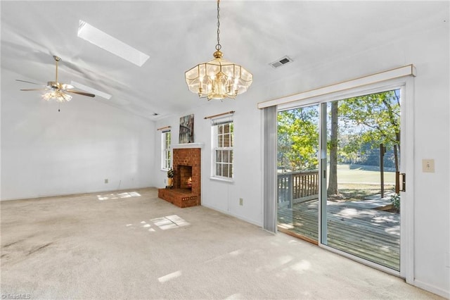 unfurnished living room with lofted ceiling with skylight, ceiling fan with notable chandelier, carpet floors, and a fireplace