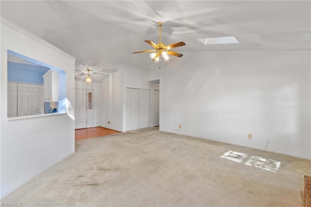 carpeted empty room with vaulted ceiling with skylight and ceiling fan