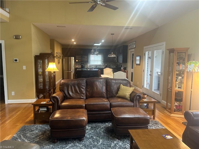 living room featuring a ceiling fan, baseboards, and light wood finished floors