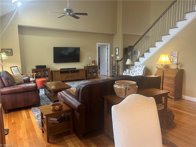 living area featuring ceiling fan, a towering ceiling, baseboards, light wood-style floors, and stairway