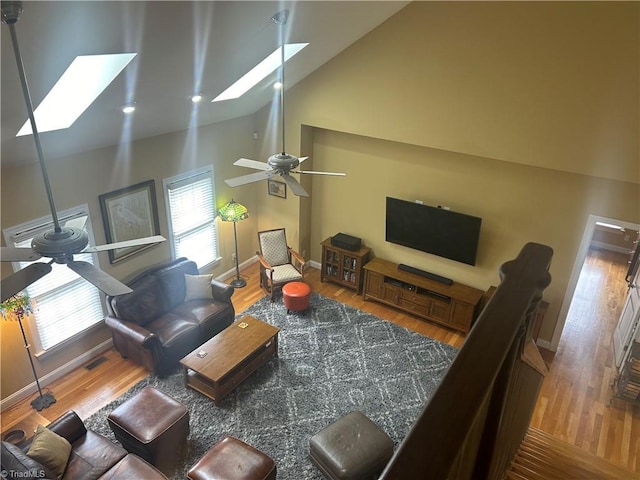 living area with ceiling fan, high vaulted ceiling, a skylight, wood finished floors, and baseboards