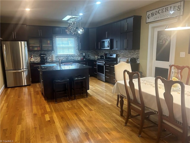 kitchen with light wood finished floors, appliances with stainless steel finishes, a breakfast bar area, and decorative backsplash