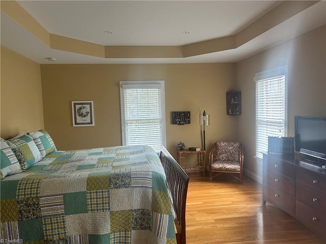 bedroom with a raised ceiling, multiple windows, light wood-style flooring, and baseboards