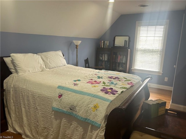 bedroom featuring lofted ceiling, visible vents, baseboards, and wood finished floors