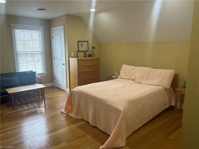 bedroom featuring lofted ceiling, wood finished floors, visible vents, and baseboards