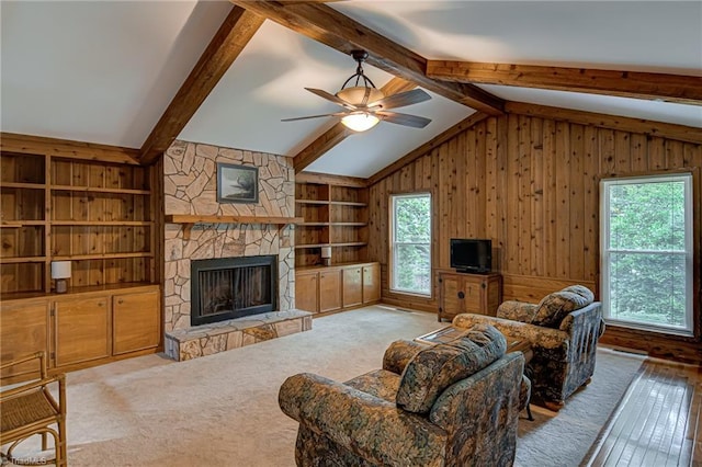 carpeted living room with built in features, lofted ceiling with beams, a fireplace, ceiling fan, and wood walls