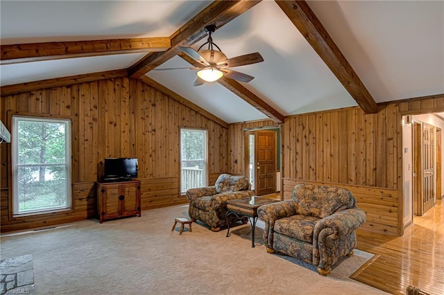 carpeted living area with wooden walls, vaulted ceiling with beams, and a ceiling fan